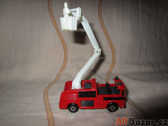 Model nákladního hasičského vozidla se zvedací plošinou ve které je hasič.